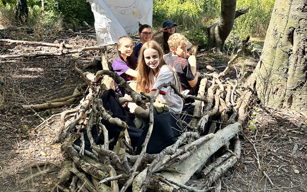 Young people in their boat built from sticks at the Make (Good) Trouble and Dragon Drama Holiday Club in Friston Forest, East Sussex